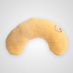 A U-shaped, fuzzy textured pillow in a warm golden-yellow color, featuring a small embroidered pink heart on the right side, set against a light gray background.