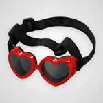Heart-shaped novelty sunglasses with bright red frames, dark lenses, and an adjustable black elastic strap, shown on a light gray background.