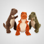 Three plush dinosaur toys made of textured cord material, shown standing side by side on a light gray background. The toy on the left is brown, the center toy is orange, and the toy on the right is olive green.