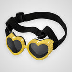Heart-shaped novelty sunglasses with bright yellow frames, dark lenses, and an adjustable black elastic strap, shown on a light gray background.